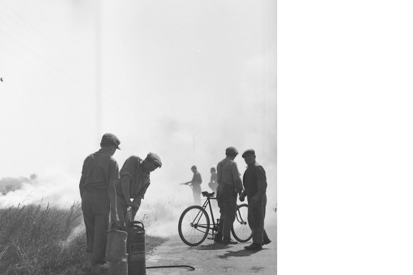 Männliche Personen mit Kappen am Rande eines Feldes, vermutlich einen Brand löschend (o. J.). Foto: Otl Aicher. © Florian Aicher Rotis, HfG-Archiv / Museum Ulm. HfG-Ar Ai F 0544.