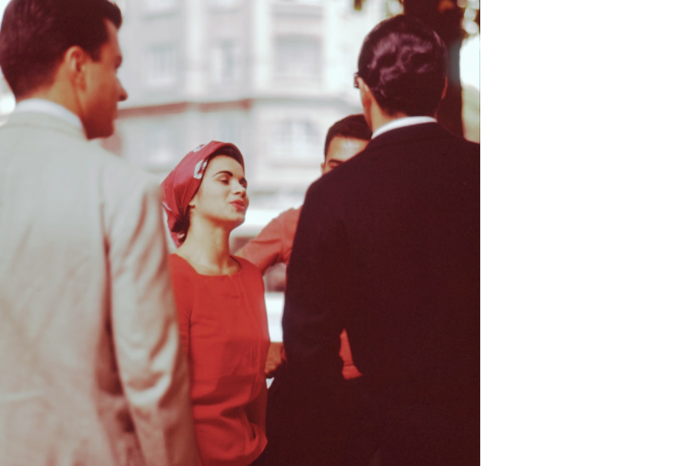Eine in Rot gekleidete Frau mit lockerem, rotem Kopftuch, umstehend männliche Personen im Anzug, vermutlich Brasilien-Reise Aicher (ca. 1950er Jahre). Foto: Otl Aicher. © Florian Aicher Rotis, HfG-Archiv / Museum Ulm. HfG-Ar Ai D 2_102.